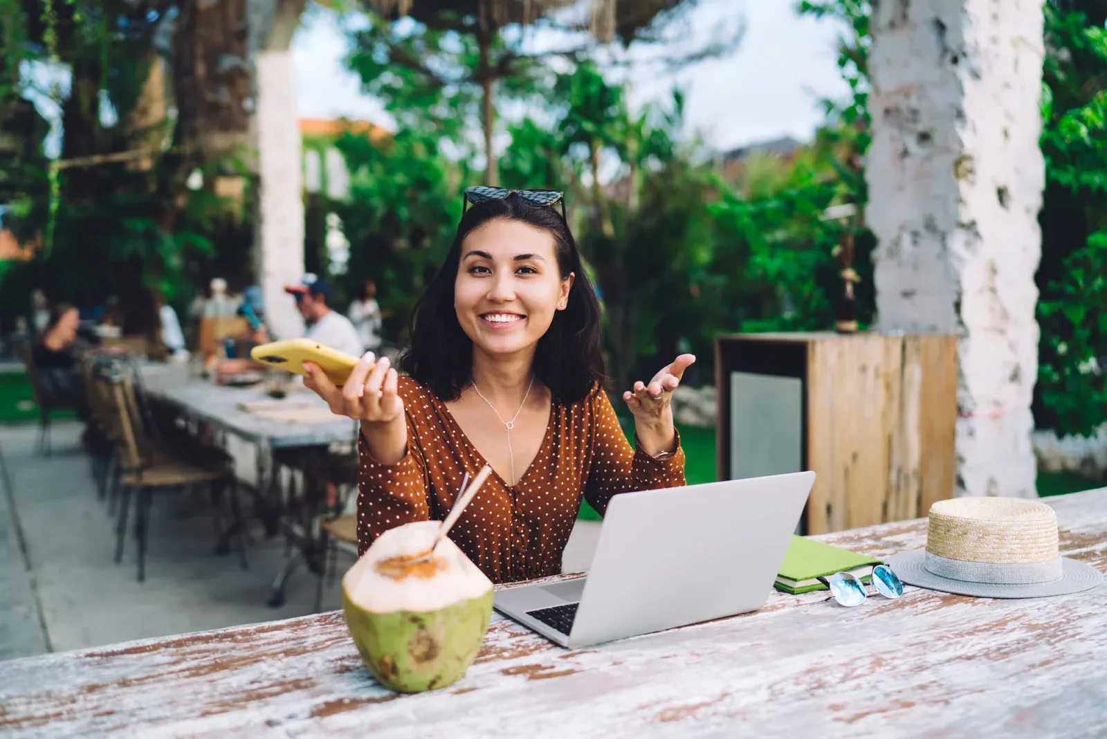 Delighted woman with smartphone and laptop working in cafe