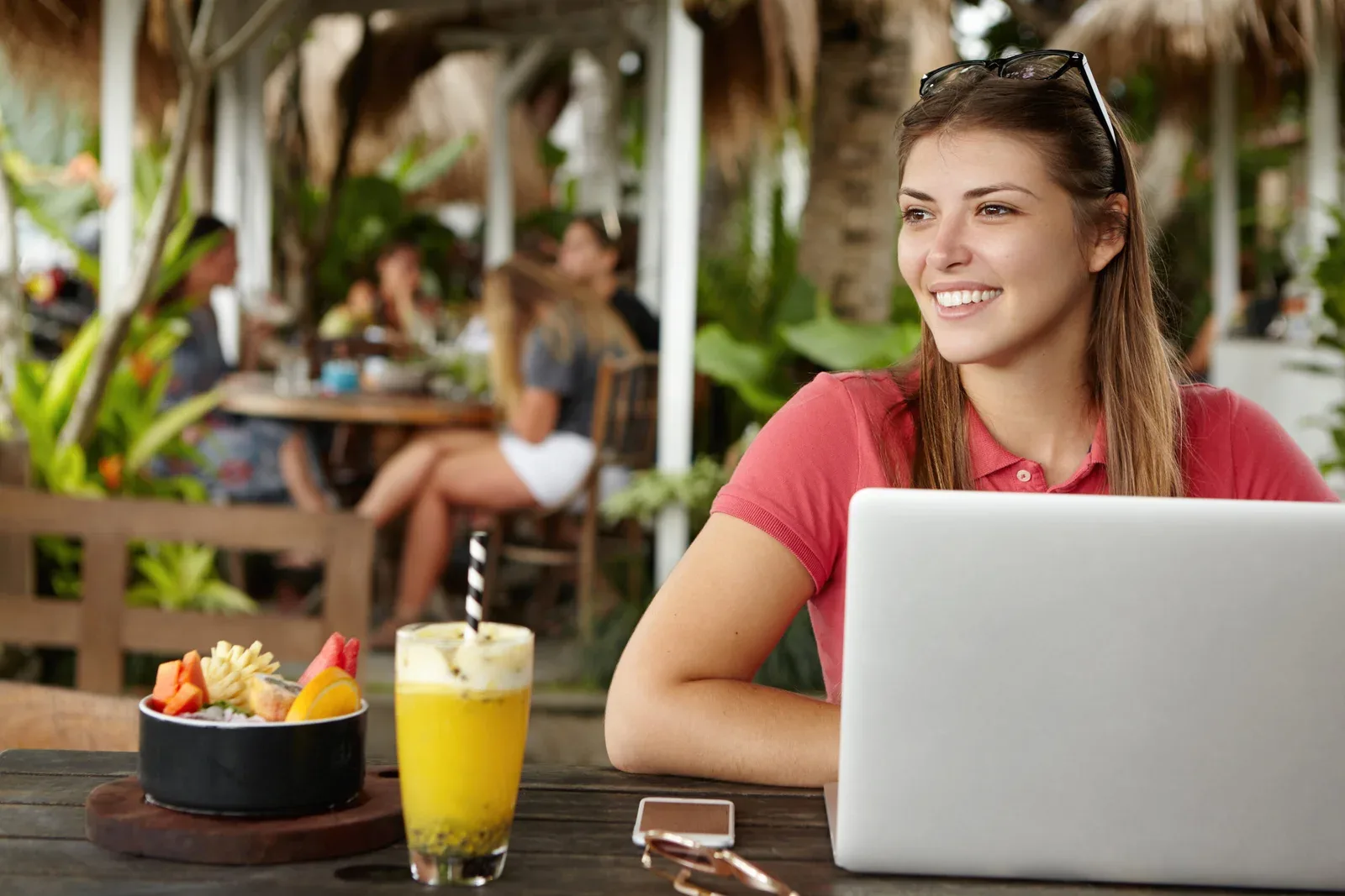 Happy young self-employed woman enjoying free wireless internet connection sitting in front of generic laptop at outdoor cafe. Joyful female using notebook computer during lunch at sidewalk restaurant